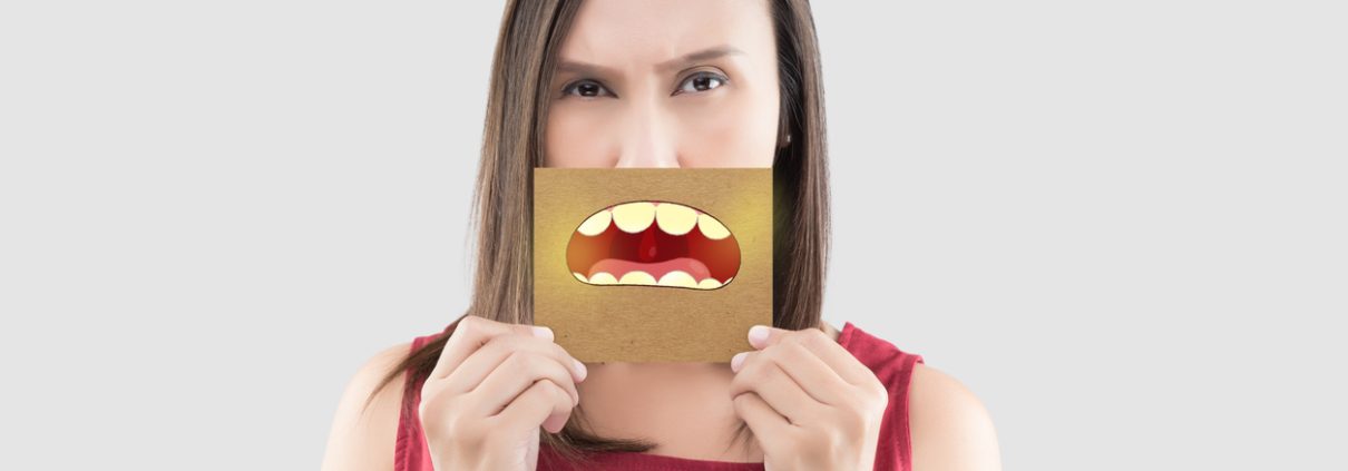 Asian woman in the red shirt holding a brown paper with the yellow teeth cartoon picture of his mouth against the gray background, Bad breath or Halitosis, The concept with healthcare gums and teeth